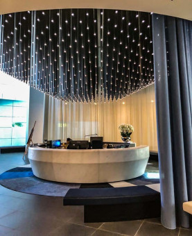 Warehouse 500 - Büroeinrichtung - München 42 Moderne Empfangstheke in einem stilvollen Foyer, umgeben von sanftem Licht und eleganten Vorhängen.