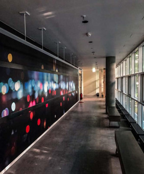 Warehouse 500 - Büroeinrichtung - München 39 Moderner Flur mit einem Wandgemälde aus verschwommenen Lichtern und großen Fenstern, die Tageslicht einlassen.