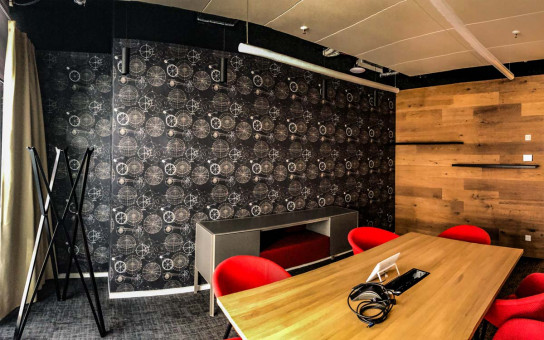 Warehouse 500 - Büroeinrichtung - München 36 Modern eingerichteter Besprechungsraum mit Holz- und grafitfarbener Wand, rotem Mobiliar und Tisch, ausgestattet mit Technik.
