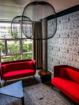 Warehouse 500 - Büroeinrichtung - München 30 Roter Lounge-Bereich mit zwei modernen Sofas und einem kleinen Tisch, umgeben von großen Fenstern und stilvollem Wanddesign.