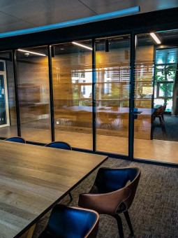 Warehouse 500 - Büroeinrichtung - München 27 Moderner Besprechungsraum mit großen Fensterfronten, Holzvertäfelung und einem Holz-Tisch, umgeben von stilvollen Stühlen.