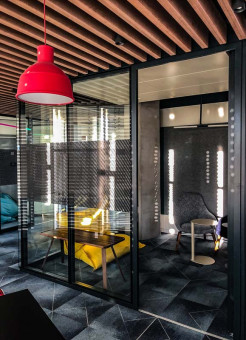 Warehouse 500 - Büroeinrichtung - München 10 Moderner, eleganter Besprechungsraum mit Glaswänden, Holzbalkendecke und bunten Möbeln. Ein roter Lampenschirm sorgt für Akzentlicht.