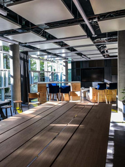 Warehouse 500 - Büroeinrichtung - München 22 Moderne Büroumgebung mit großen Fenstern, Holz-Tisch und Stühlen in einem hellen Raum, ideal für kreative Meetings.