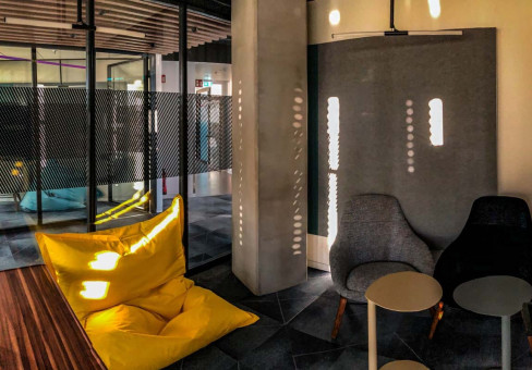 Warehouse 500 - Büroeinrichtung - München 9 Gemütliche Sitzecke mit einem gelben Sitzsack, grauen Stühlen und Tischen, durch Fenster einfallendes Licht schafft eine einladende Atmosphäre.