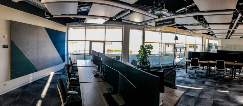 Warehouse 500 - Büroeinrichtung - München 44 Moderne Bürolandschaft mit mehreren Schreibtischen, großen Fenstern und viel Tageslicht, ergänzt durch Pflanzen und stilvolle Trennwände.