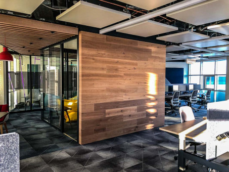 Warehouse 500 - Büroeinrichtung - München 12 Moderne Büroszene mit einem gläsernen Besprechungsraum, Holzverkleidung und ergonomischen Arbeitsplätzen in einem offenen Raum.