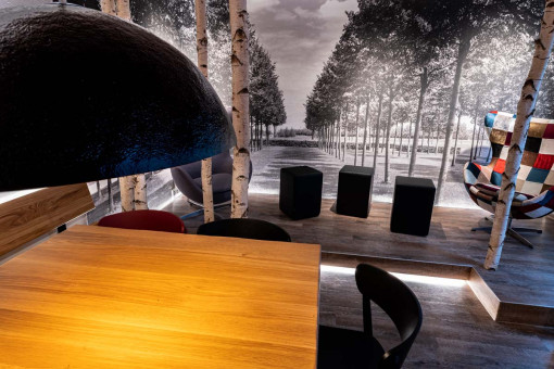 May Landschaftsbau - Büroeinrichtung - Feldkirchen 10 Moderne Einrichtung mit einem Holz-Tisch und schwarzen Stühlen, umgeben von einer künstlerischen Wandgestaltung mit Naturmotiven.