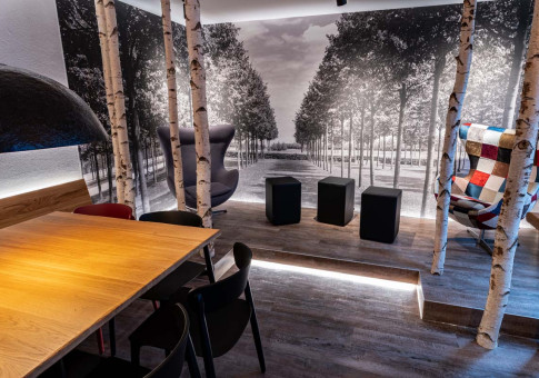 May Landschaftsbau - Büroeinrichtung - Feldkirchen 7 Moderne Raumgestaltung mit Holzdekor, sitzenden Möbeln und einer eindrucksvollen Schwarz-Weiß-Wand mit Baumansicht.