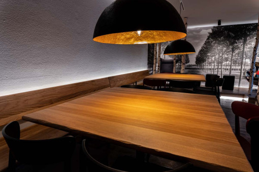 May Landschaftsbau - Büroeinrichtung - Feldkirchen 38 Holztisch in einem modern eingerichteten Restaurant mit warmen Licht von stilvollen Lampen und einer minimalistischen Wanddekoration.