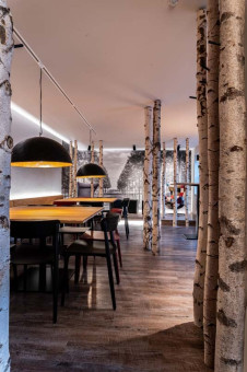 May Landschaftsbau - Büroeinrichtung - Feldkirchen 37 Modernes Restaurant mit eleganten Möbeln, gestalteten Wänden und Birkenstämmen als Deko-Elementen, die eine natürliche Atmosphäre schaffen.