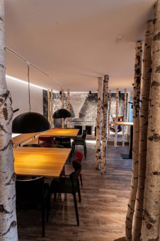 May Landschaftsbau - Büroeinrichtung - Feldkirchen 35 Gemütlicher Restaurantbereich mit Holztischen und Birkenstamm-Säulen, umgeben von stilvollen Stühlen und modernem Dekor.
