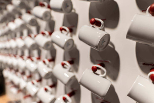 May Landschaftsbau - Büroeinrichtung - Feldkirchen 32 Weiße Kaffeetassen mit roten Henkel, an einer Wand hängend, in regelmäßigen Abständen angeordnet.