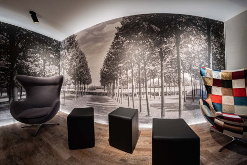 May Landschaftsbau - Büroeinrichtung - Feldkirchen 30 Moderne Lounge mit stilvollem Sessel und quadratischen Hockern vor einer schwarz-weißen Baumfotografie.