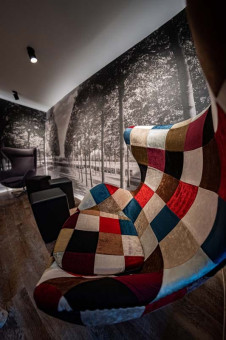 May Landschaftsbau - Büroeinrichtung - Feldkirchen 28 Bequemer Sessel mit farbenfrohem, quadratischem Muster vor einer schwarz-weiß Fototapete einer Baumallee.