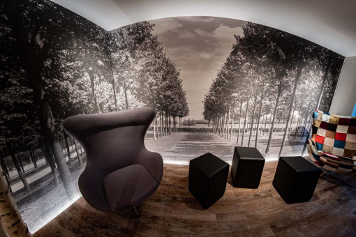 May Landschaftsbau - Büroeinrichtung - Feldkirchen 27 Moderne Inneneinrichtung mit einem schwarzen Sessel, stilvollen Würfeln und einer monochromen Waldmauer im Hintergrund.
