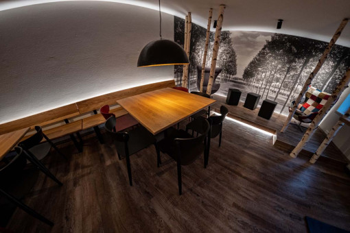 May Landschaftsbau - Büroeinrichtung - Feldkirchen 23 Moderne Restaurant-Innenansicht mit Holzstühlen und einem großen Tisch unter einer eleganten Pendelleuchte.