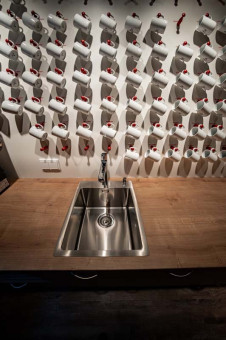 May Landschaftsbau - Büroeinrichtung - Feldkirchen 21 Moderne Küchenspüle aus Edelstahl in einem Holzunterschrank, umgeben von zahlreichen weißen Kaffeetassen an der Wand.