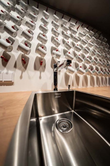 May Landschaftsbau - Büroeinrichtung - Feldkirchen 19 Moderne Spüle aus Edelstahl mit ausgeklügeltem Wasserhahn, im Hintergrund eine Wand mit vielen Kaffeetassen.