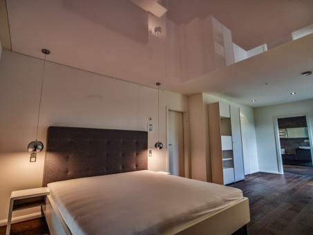 Schlafzimmer mit spiegelnder Decke und dunklem Parkettboden und weißen Wänden