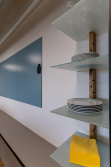 Holzregal mit Glasböden und Tellern darin. Dahinter ein Whiteboard in blau