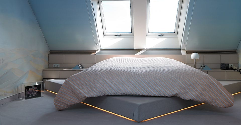 Schlafzimmer mit einem Bett unter einer Dachschräge welches auf einem Dreieck steht