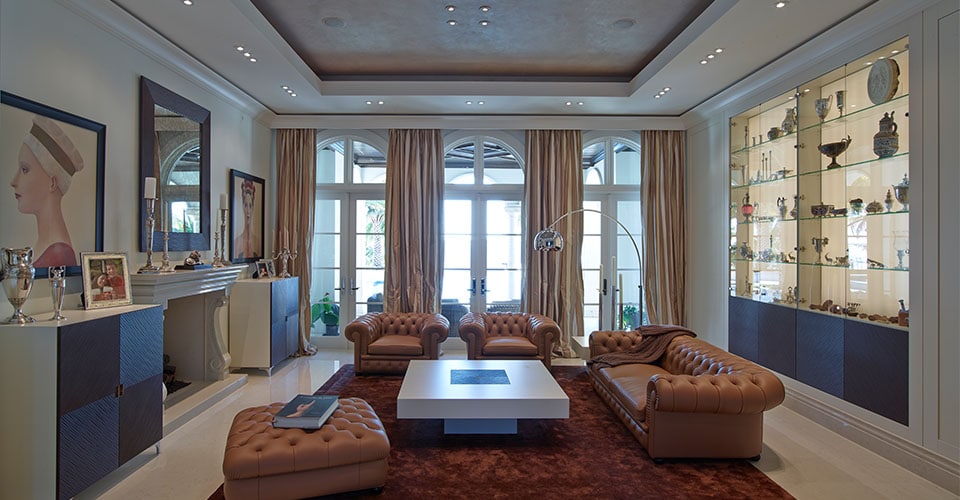 Kaminzimmer mit braunem Echtleder Sofa raumhohen Stoffvorhängen und Deckenfries mit Licht