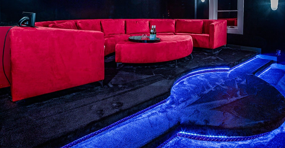 Heimkino mit großer roter Couch in einem  mit blauer Beleuchtung auf blauem Teppich