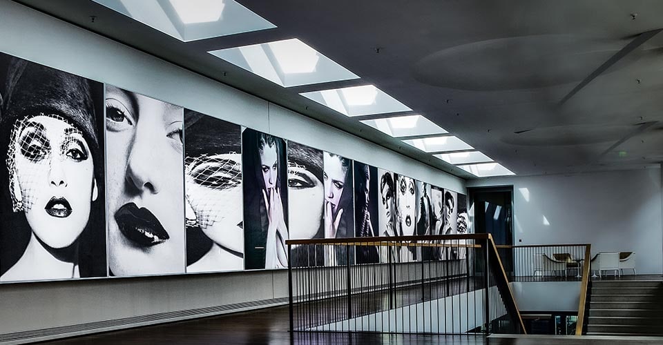 Treppenaufgang mit einer gesamten Wand aus Lichtkästen mit Fotos in schwarzweiß