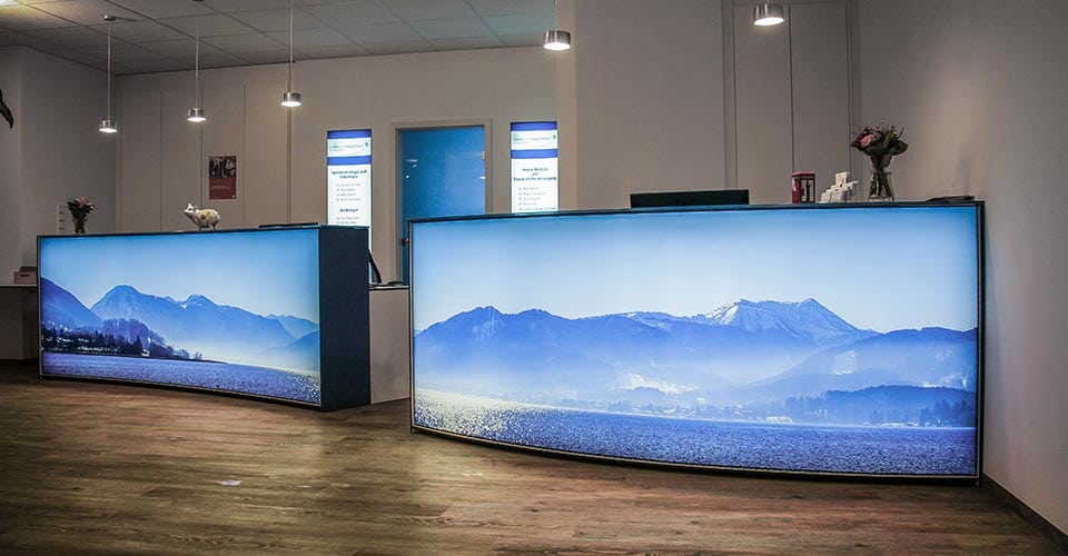 Tresen in der Gemeinschaftspraxis Medicum am Tegernsee mit zwei großen Lichtkästen, auf denen der Tegernsee zu sehen ist