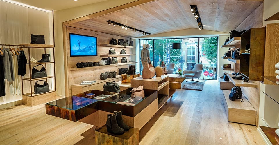 Geschäft mit Holzwänden und Glasfront mit Schuhen und Taschen als Beispiel für Ladenbau Mode