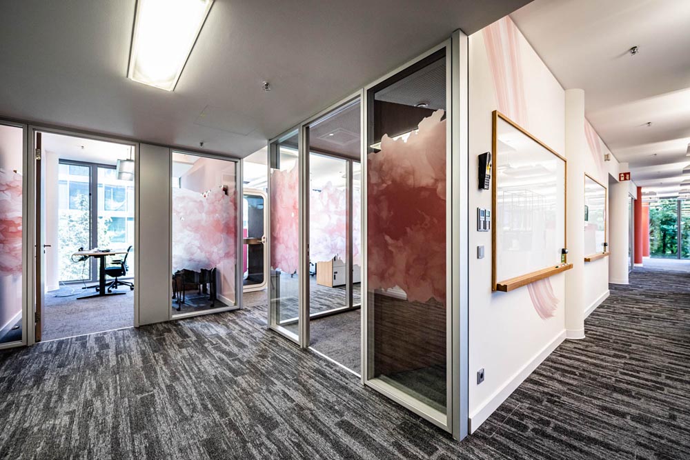 Bild mit vielen kleinen Einzelbüros in Designoffice mit Teppichboden und Whiteboards an den Wänden. Bürowände als Glastrennwände mit künstlerischer Folierung in München
