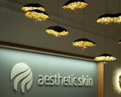 Detailaufnahme goldener Pendelleuchten vor unscharfem Praxis-Logo „aesthetic skin“