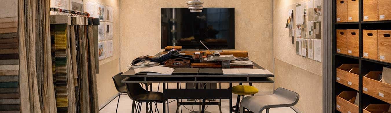 Bemusterungs- und Besprechungsraum mit großem Tisch, Materialmustern, Stoffkollektionen, Musterregalen und integrierter Medientechnik – individuell geplant und umgesetzt von einer Schreinerei München.