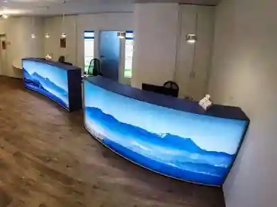 Schreinerei München - Arve Einrichtung GmbH 26 Praxiseinrichtung mit halbrunder Tresenanlage und bedruckter Gewebefolie hinterleuchtet und Motiv mit blauen Bergen