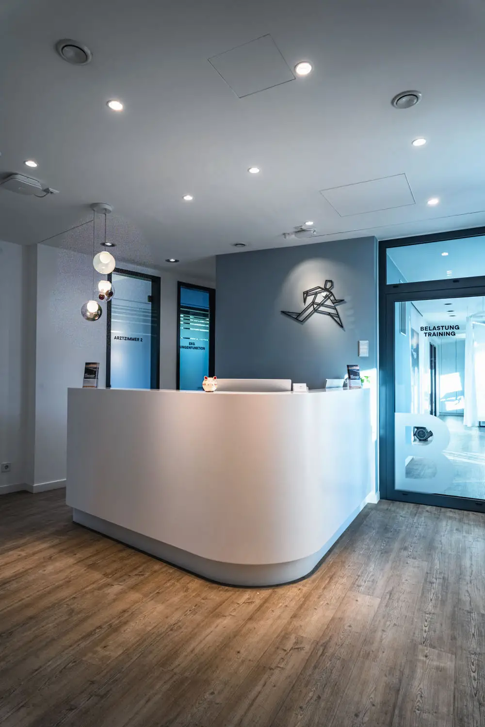 Empfangsbereich einer Arztpraxis mit abgerundetem Tresen, Beleuchtung und Glasflur